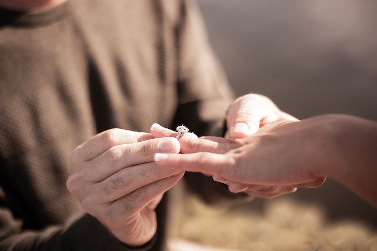 man putting engagement ring on fiancee's finger